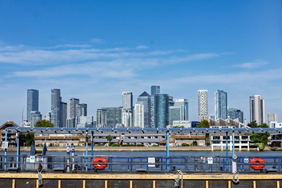 A city skyline featuring a mix of modern high-rise office buildings made of glass and steel, with reflective surfaces and varying heights, dominates the background. In the foreground, a row of low-ris